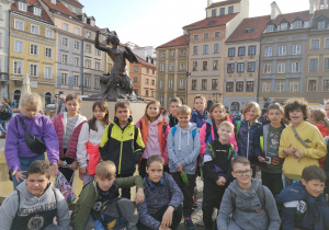 grupa dzieci stoi przed pomnikiem Syrenki na Starym Mieście w Warszawie