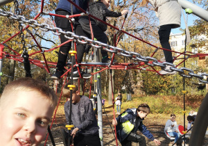 Na zdjęciu dzieci wspinają się na linowym labiryncie, jeden z chłopców patrzy na osobę wykonującą zdjęcie.