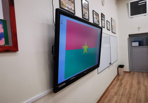 Na zdjęciu widać ekran z wyświetloną flaga i białą tablice. Zdjęcie wykonano z boku w sali lekcyjnej.