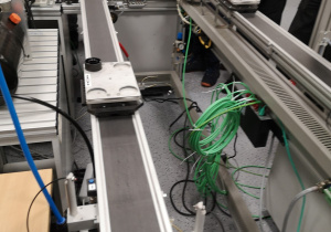 Zdjęcie przedstawia zautomatyzowaną linię produkcyjną, na której widać platformy przewożące plastikowe części do składania.