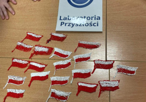 Na ławce leżą flagi Polski wykonane długopisami 3d oraz logo "Laboratoria Przyszłości"