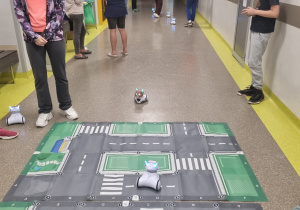Grupa dzieci steruje robotami na makiecie miasteczka drogowego.