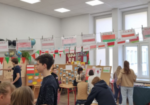 Na zdjęciu widać salę szkolną. Nad głowami dzieci wiszą przyczepione do sznurka flagi Białorusi. Widać tablice z plakatami, dzieci oglądające wystawę.
