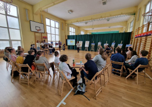 Na sali gimnastycznej widać delegacje szkół zaproszonych do udziału w projekcie. W głębi wystawa zdjęć przedstawiających budynki i miejsca Łodzi.