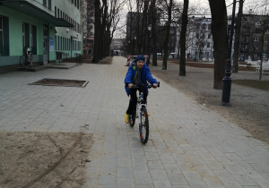 Jeden z uczniów jedzie rowerem po alejce parkowej.
