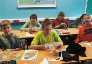 W sali lekcyjnej uczniowie siedzą w ławkach. Na stole widać karty pracy, na których narysowany jest plan mózgu. Uczniowie wycinają karty.