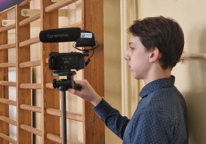 Na zdjęciu uczeń stoi przy kamerze. Na kamerze widać logo programu "Laboratoria Przyszłości"