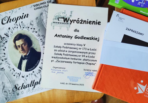 Po lewej stronie znajduje się portret Chopina, w środku dyplom dla uczennicy naszej szkoły, po prawej koperta z zaproszeniem oraz czerwony folder z napisem "50 lat chóru Filharmonii Łódzkiej"