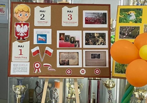 Na zdjęciu na korytarzu szkolnym stoi tablica z dekoracją na święta majowe
