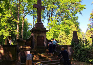 Na zdjęciu widać grób na cmentarzu Ogrodowa. Widać również chłopców sprzątających pomnik i miejsce wokół.