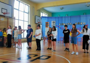 Na sali gimnastycznej stoją w rzędzie wszyscy uczniowie biorący udział w przedstawieniu.