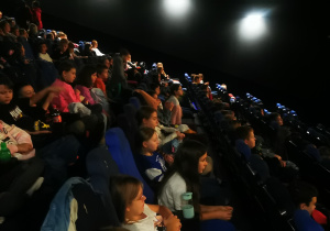 Na zdjęciu widać dzieci siedzące w sali kinowej