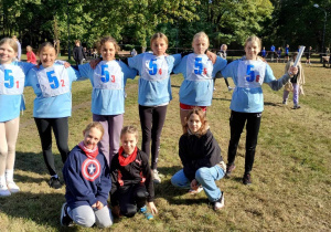 Na trawie stoją uczestniczki biegów przełajowych reprezentujące naszą szkołę. Dziewczynki ubrane są w jednakowe niebieskie koszulki