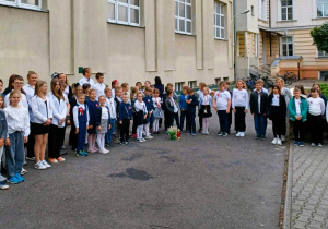 Na dziedzińcu szkolnym stoją uczniowie zebrani na uroczystym apelu