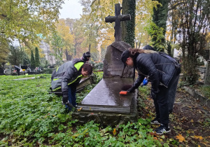 Na zdjęciu widać dwoje uczniów sprzątających grób na Starym Cmentarzu