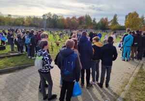 Na zdjęciu młodzież zgormadzona na cmentarzu. Na dalszym planie widać drewniane krzyże.