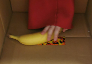 Na zdjęciu widać środek pudełka, w którym leży banan. Widać rękę dziecka trzymającą owoc.