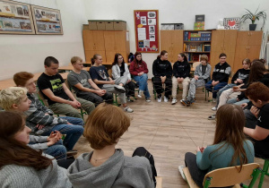 Na środku sali lekcyjnej w kręgu na krzesełkach siedzą uczniowie. W rękach trzymają sznurek, który ma kształ pajęczyny.