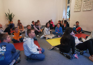 W pomieszczeniu uczniowie w grupach siedzą na podłodze.