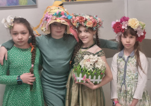 Na zdjęciu cztery dziewczynki ubrane w zielone ubrania. Trzy z nich na głowie mają kapelusze z kwiatami.