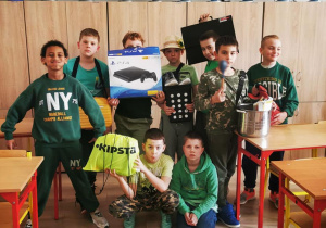 W sali szkolnej grupowe zdjęcie chłopców prezentujących zielone stroje i zamienniki plecaków szkolnych.