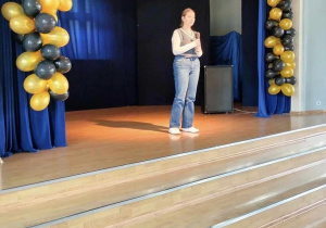 Na scenie udekorowanej balonami widać stojącą uczennicę naszej szkoły