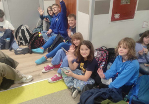 Na szkolnym korytarzu siedzą uczniowie w ubraniach w kolorze niebieskim.
