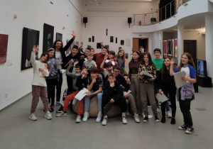 Zdjęcie grupowe uczniów biorących udział w zajęciach projektowych w Miejskiej Galerii Sztuki. W tle na ścianach wiszą obrazy.