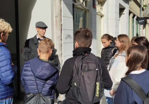 Grupa uczniów naszej szkoły stoi przed bramą jednej z kamienic. Widać osobę prowadzącą grę miejską.